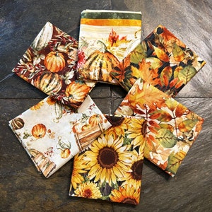 May include: Six fabric squares with autumnal themes. The squares feature pumpkins, sunflowers, leaves, and other fall motifs in shades of orange, yellow, brown, and green.