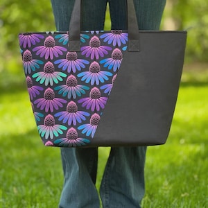 May include: The Tango Tote bag, featuring a floral pattern in shades of purple, blue, and teal on a black background. The tote has a solid black side and handles. The bag is approximately 12 inches high, 18 inches wide at the top, and 7 inches deep.