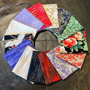 May include: A collection of folded fabric squares in various colors and patterns, arranged in a circular shape. The fabrics feature floral, geometric, and abstract designs, with colors including red, gold, blue, and purple. The fabrics are likely suitable for quilting or crafting projects.