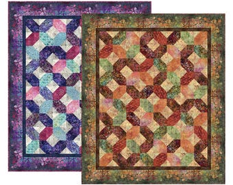 May include: Two rectangular quilts featuring a geometric interlocking pattern. The left quilt displays shades of purple, blue, and pink with a floral border. The right quilt features warm tones of orange, red, and green with a dark brown border.