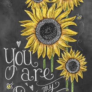 May include: Chalkboard art with a black background and white text that reads "you are my sunshine". The text is surrounded by four yellow sunflowers with green stems. There are also small bee illustrations.