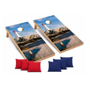 May include: Two rectangular wooden cornhole boards featuring a printed image of a white lighthouse on a rocky coastline with a blue sky. Each board has a circular hole at the top. Includes three solid red fabric bean bags and three solid blue bags.