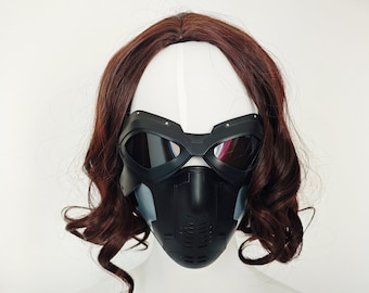 Può includere: Una maschera facciale nera con una visiera trasparente e un design testurizzato. La maschera ha un cinturino nero che va intorno alla testa.