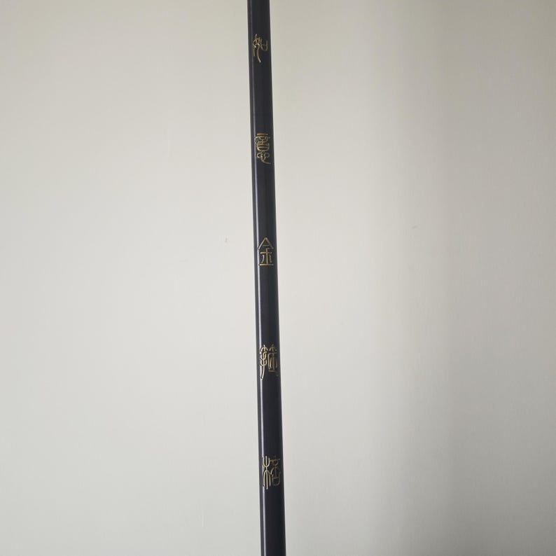 May include: A black wooden stick with gold lettering. The lettering reads "金", "龍", "鳳", and "龍".