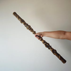 May include: A long, ornate, gold-colored staff with intricate carvings. The staff is held by a hand in the image.