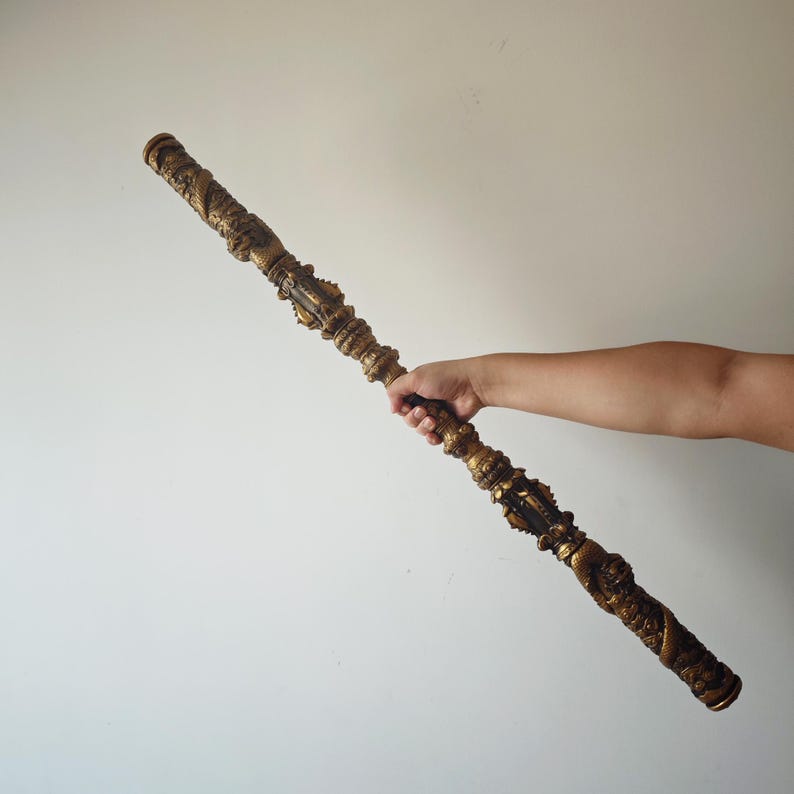 May include: A long, ornate, gold-colored staff with intricate carvings. The staff is held by a hand in the image.