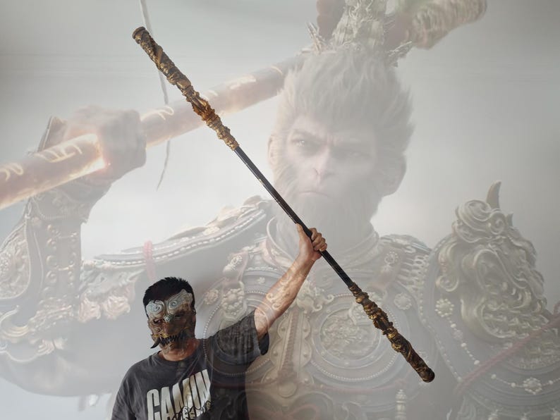 May include: A person holding a long, black and gold staff with intricate details. The staff is decorated with gold accents and has a pointed tip. The staff is held in front of a mural depicting a monkey warrior with a golden crown and armor.