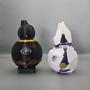 May include: Two decorative spherical objects. One is black with gold accents and a dragon design, the other is white with black and gold details. Both have unique, geometric shapes and stand on small bases.