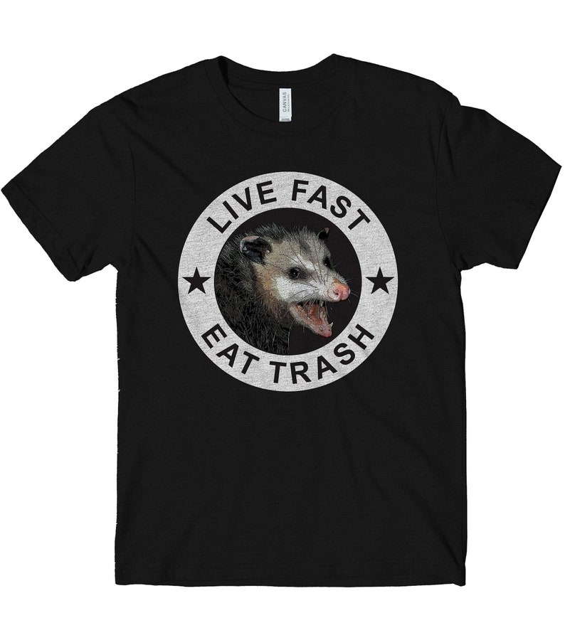 May include: Black t-shirt with a white circle graphic featuring a possum with its mouth open and the text "Live Fast Eat Trash".