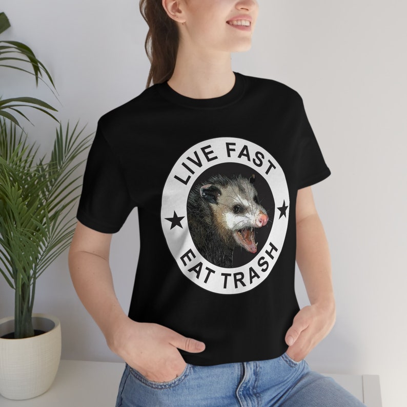 May include: Black t-shirt with a white circle graphic featuring a possum and the text "Live Fast Eat Trash".