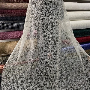 May include: White sheer fabric with a pattern of small white circles. The fabric is draped over a roll of fabric.