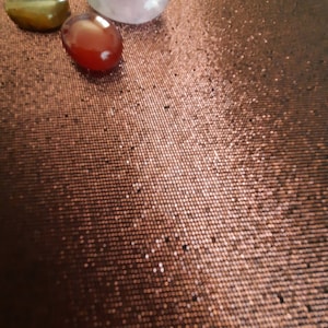 May include: Three smooth stones on a brown textured surface. The stones are a light purple, a dark red, and a brown with gold flecks.