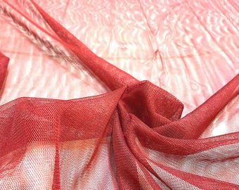 May include: A sheer, deep red mesh fabric with a fine, uniform hexagonal grid pattern. The material is draped in soft, flowing folds, revealing a translucent quality that allows light to pass through the delicate, lightweight, and porous textile.