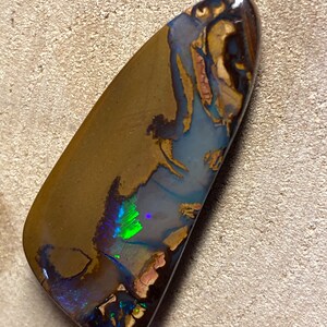 May include: A brown, green, and blue opal gemstone with a teardrop shape. The opal has a natural, rough surface and is set in a silver bezel.