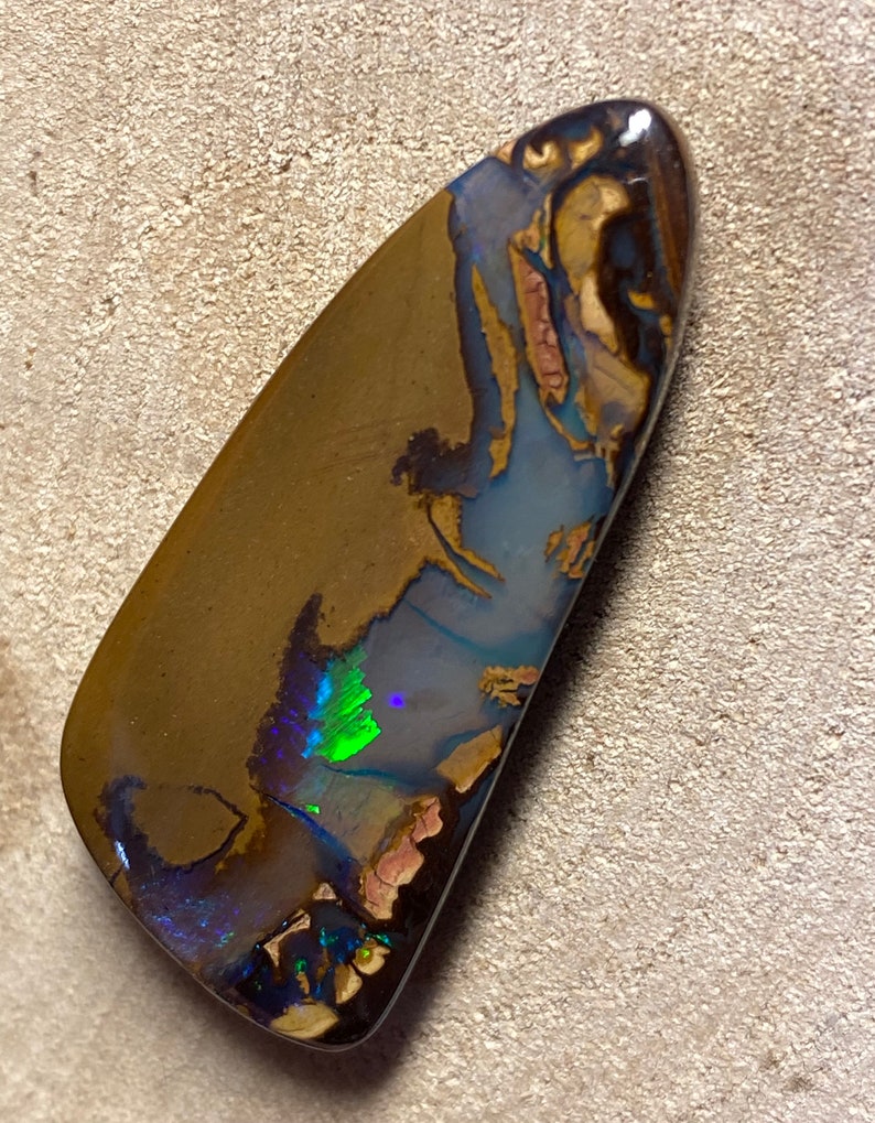 May include: A brown, green, and blue opal gemstone with a teardrop shape. The opal has a natural, rough surface and is set in a silver bezel.