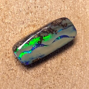 May include: A green, blue and black opal cabochon with a silver backing. The opal has a wavy pattern and is set in a rectangular shape.