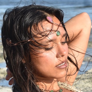 以下が含まれることがあります： 銅線で作られたヘアバンドで、片側にスパイラルデザイン、宝石のアクセントが付いています。 ピンクとグリーンの宝石が特徴で、額に着用します。