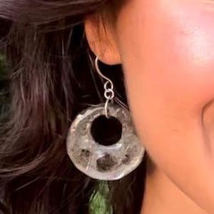 May include: Silver hoop earrings with a clear resin design featuring a silver circle in the center.