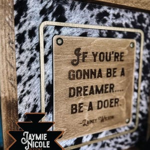 May include: Wooden framed sign with a cowhide pattern background. The sign features a wooden plaque with the quote "If you're gonna be a dreamer... be a doer." The sign also includes the text "Jaymie Nicole Designs."
