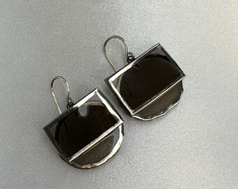 May include: A pair of silver earrings with a semi-circular shape and a black glass insert. The earrings have a simple, modern design.