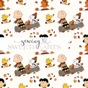 Könnte beinhalten: Ein weißer Stoff mit einem sich wiederholenden Muster aus Peanuts-Figuren wie Charlie Brown, Snoopy, Woodstock und Lucy in Herbstkleidung. Das Design zeigt braune Baumstämme, orangefarbene Kürbisse und verstreute Herbstblätter.