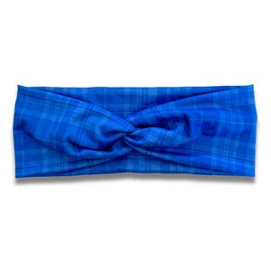 May include: A bright blue headband featuring a subtle, darker blue plaid pattern. The fabric is gathered in the centre to create a twisted knot effect, providing a textured appearance across the entire surface of the accessory.
