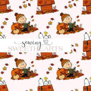 May include: A repeating pattern on a light pink background featuring a cartoon character wearing an orange beanie and scarf, reading a book while sitting among pumpkins and autumn leaves, with a dog house and a small yellow bird also present.