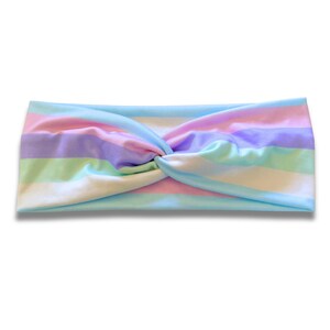 May include: A fabric headband featuring a horizontal striped pattern in pastel shades of light blue, soft pink, lavender, and mint green. The headband has a central twist detail that gathers the fabric, creating a soft, layered appearance.