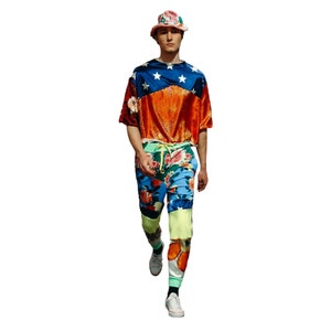 May include: A person wearing a red, white, and blue patterned shirt with a floral print on the pants. The person is wearing a pink and white hat.