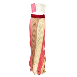 May include: A crochet two-piece set with a pink, beige, and white striped skirt and a matching cropped top. The skirt has a fringe hem and the top has a velvet waistband.
