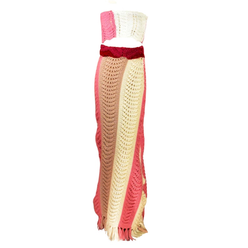 May include: A crochet two-piece set with a pink, beige, and white striped skirt and a matching cropped top. The skirt has a fringe hem and the top has a velvet waistband.