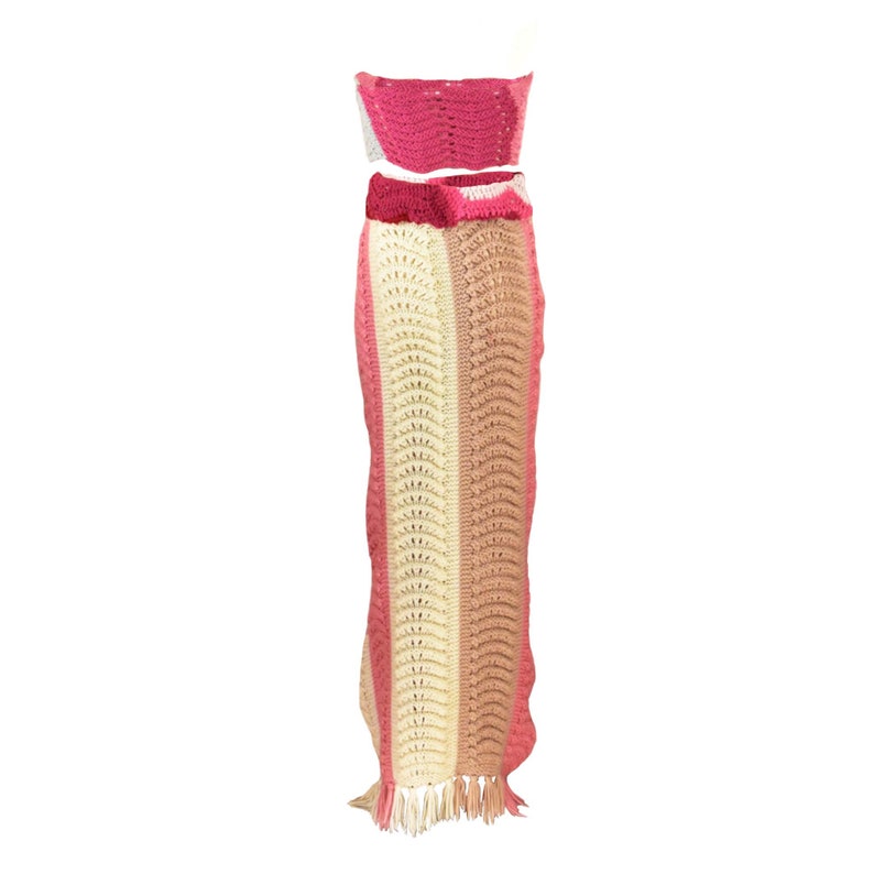 May include: A crochet two-piece outfit with a pink and cream striped skirt and a matching pink crop top.