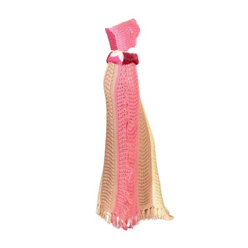 May include: A crocheted skirt and top set in pink, beige, and cream with a fringe trim. The skirt is long and flowing, and the top is a bandeau style.