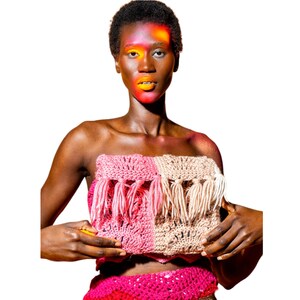 May include: A pink and beige crochet top with fringe detailing. The top is strapless and has a cropped length.