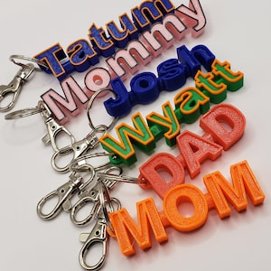 May include: A set of colorful 3D printed keychains with names like Tatum, Mommy, Josh, Wyatt, Dad, and Mom. Each keychain has a silver key ring.