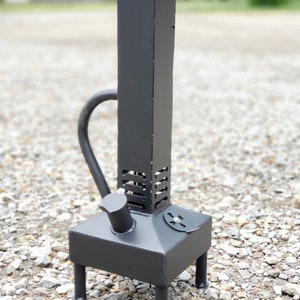 Op de afbeelding: Een zwarte metalen rookoven met een hoge schoorsteen en een kleine vuurhaard. De rookoven heeft een ronde opening aan de zijkant en vier poten.