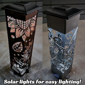 Two solar garden posts at night: one illuminated with intricate cutout patterns, the other unlit with detailed steel designs.