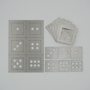 May include: A set of metal stencils for making dice. The stencils are arranged in a grid pattern, with each stencil showing a different number of dots. There are also individual stencils for each number of dots.