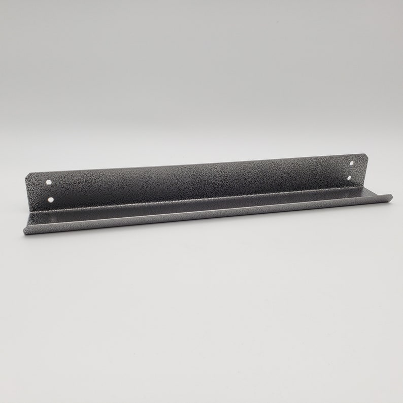 May include: A gray metal shelf with a textured finish and rounded edges. The shelf is designed to be mounted on a wall.