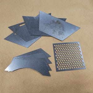 May include: A set of metal sheets in various shapes and sizes, including a sheet with a honeycomb pattern. The sheets are gray and have a metallic finish.