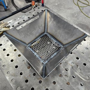 以下が含まれることがあります： 底に六角形のワイヤーメッシュグリルが付いた正方形の金属製ファイヤーピット。ファイヤーピットはスチール製で、ダークグレーの仕上げです。