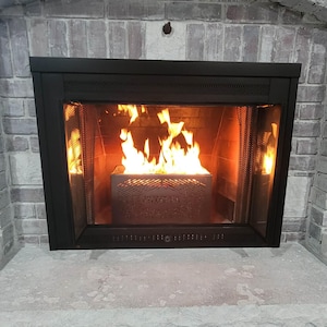 May include: A black fireplace with a roaring fire inside. The flames are bright orange and yellow, and the firebox has a decorative metal screen. The fireplace is set against a brick wall.