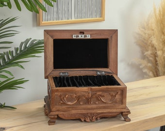 May include: A wooden jewelry box with intricate carvings and a black velvet interior. The box is open and has multiple compartments for storing jewelry.