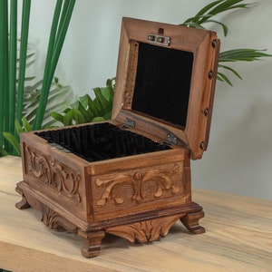 Op de afbeelding: Een houten doos met ingewikkelde houtsnijwerk en een zwart fluwelen interieur. De doos is open en heeft een scharnierend deksel.