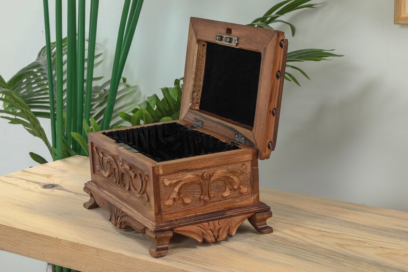 Op de afbeelding: Een houten doos met ingewikkelde houtsnijwerk en een zwart fluwelen interieur. De doos is open en heeft een scharnierend deksel.