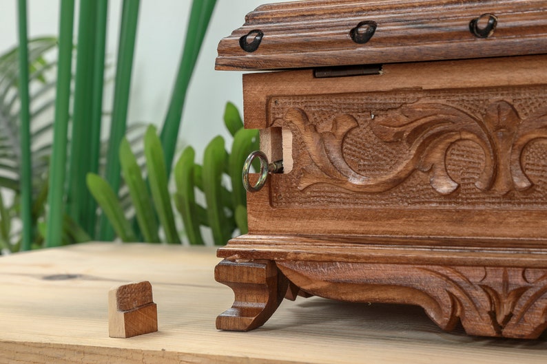 Op de afbeelding: Een houten kist met ingewikkelde houtsnijwerk en een sleutelgat. De kist is gesloten en heeft een donkerbruine afwerking. De kist staat op een houten oppervlak.