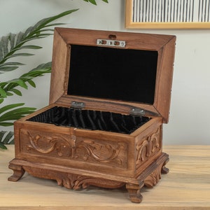 Op de afbeelding: Een houten doos met ingewikkelde houtsnijwerk en een zwart fluwelen interieur. De doos is open en het deksel is opengeklapt.