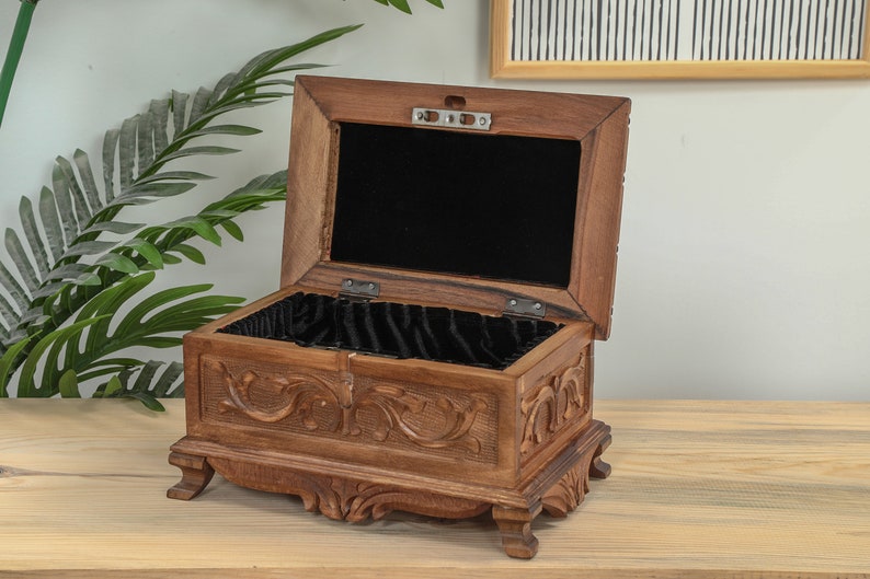 Op de afbeelding: Een houten doos met ingewikkelde houtsnijwerk en een zwart fluwelen interieur. De doos is open en het deksel is opengeklapt.