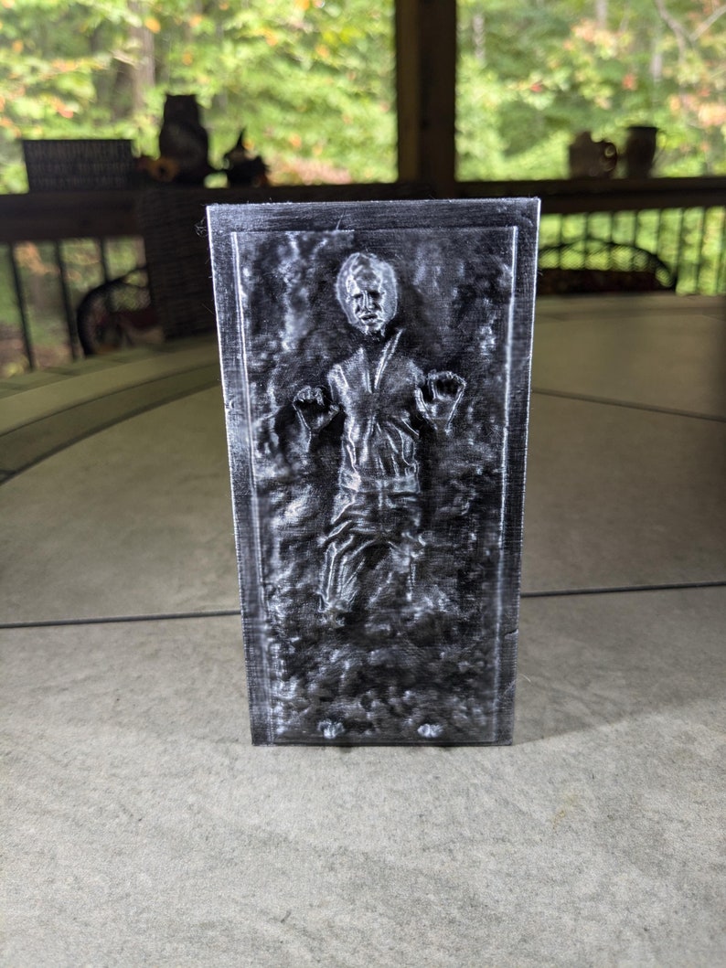 May include: A black and white 3D printed model of a person frozen in carbonite. The model is a popular character from the Star Wars franchise.