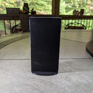 May include: A black chalkboard sign with a rounded base. The sign is blank and ready to be written on.